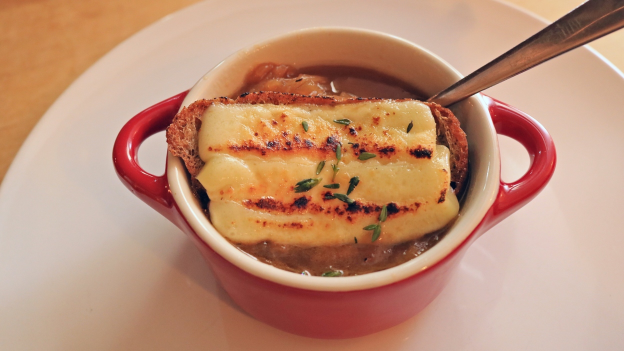 A small red crock full of French onion soup.