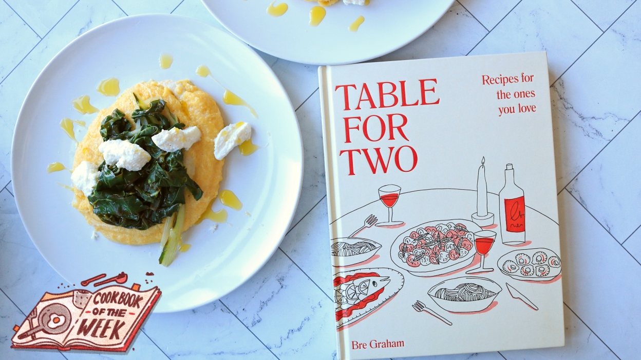 A cookbook on a table with a plate of polenta and greens.