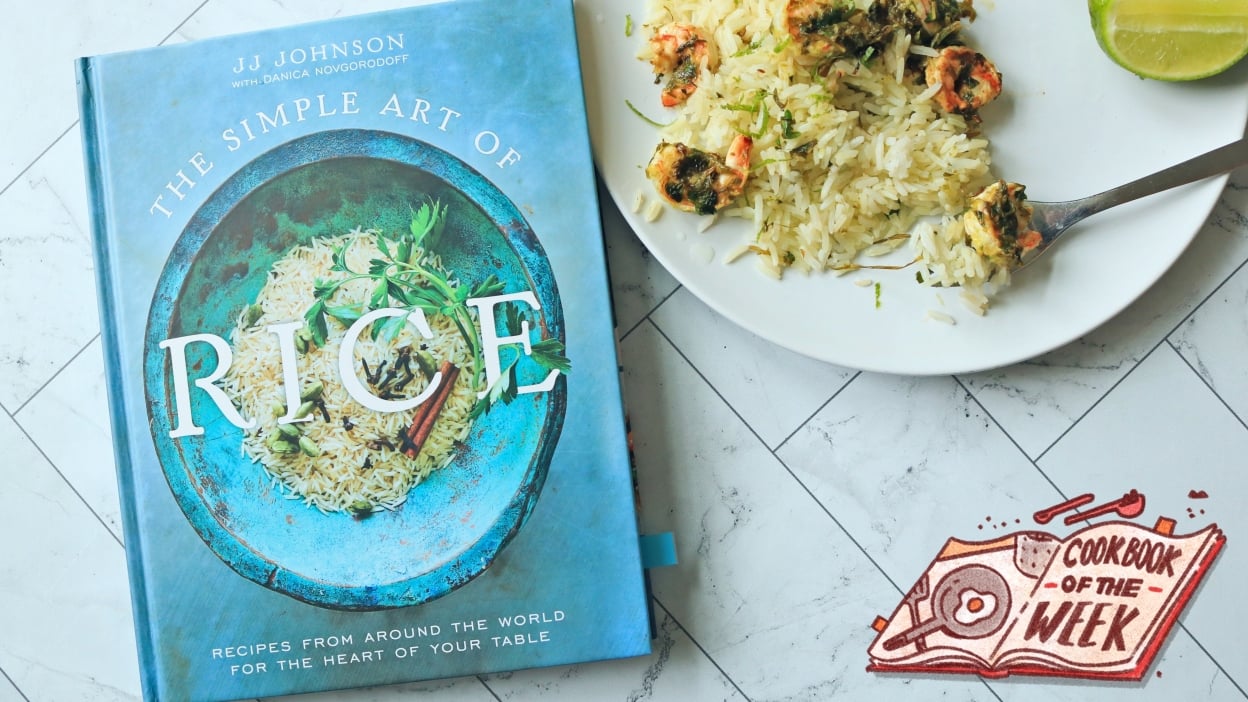 The Simple Art of Rice cookbook on a table with a plate of shrimp and rice.