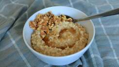 A bowl of steel cut oatmeal with honey and walnuts sits on a tablecloth.