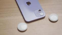 A purple iPhone sitting on a wood table next to two circular AirTag devices