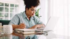 Woman working at laptop, taking notes.