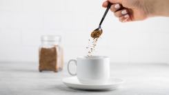 A hand dropping instant coffee into a mug