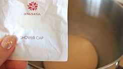 A hand holding a small packaged hotel shower cap in front of a bowl of dough.