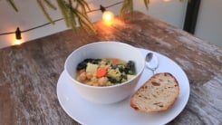 A bowl of soup with bread on a table with outdoor lights.