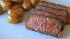 Steak slices next to baby potatoes on a plate.