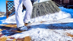 person using broom to sweep snow off sidewalk
