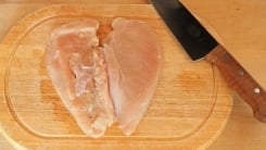 A butterflied raw chicken breast o a cutting board with a carving knife.