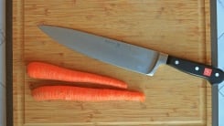 A chef's knife on a cutting board with two carrots.