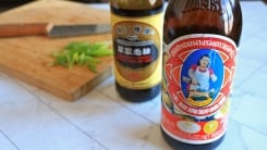 Two bottles of Asian seasoning sauce in front of a cutting board.