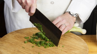 Close-up of chef's hands cutting scallions with a cleaver.