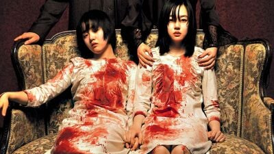 Two bloody sisters sit on a couch in a still from A Tale of Two Sisters
