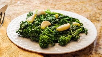 A plate of cooked broccoli rabe with garlic cloves.