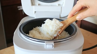 A person with a wooden spoon scooping white rice out of a cooker.
