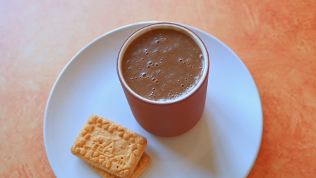Chocolate champurrado in a cup on a plate with two cookies.
