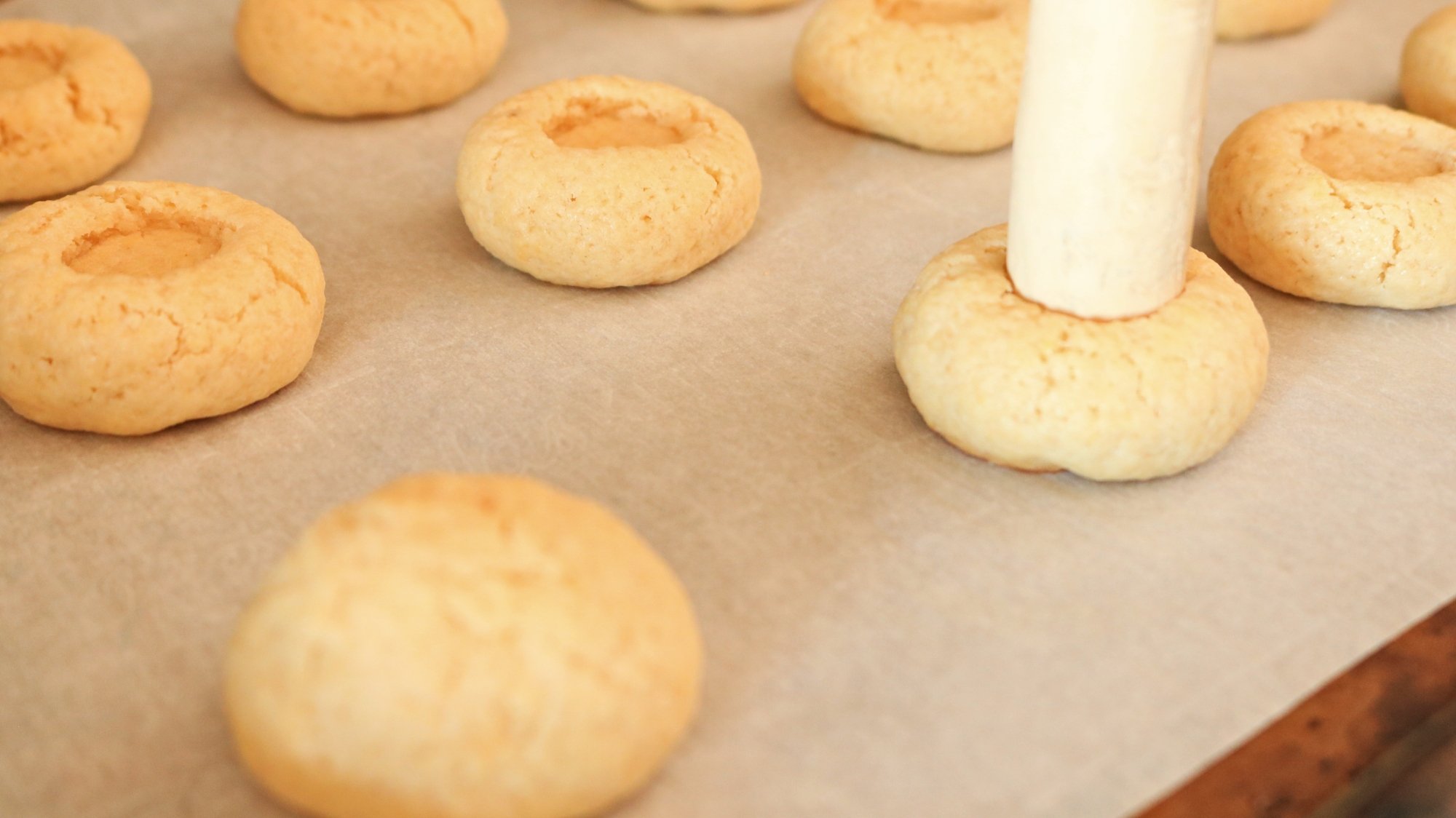 A close up of a wine cork poking a cookie and other cookies with an indent in the center.