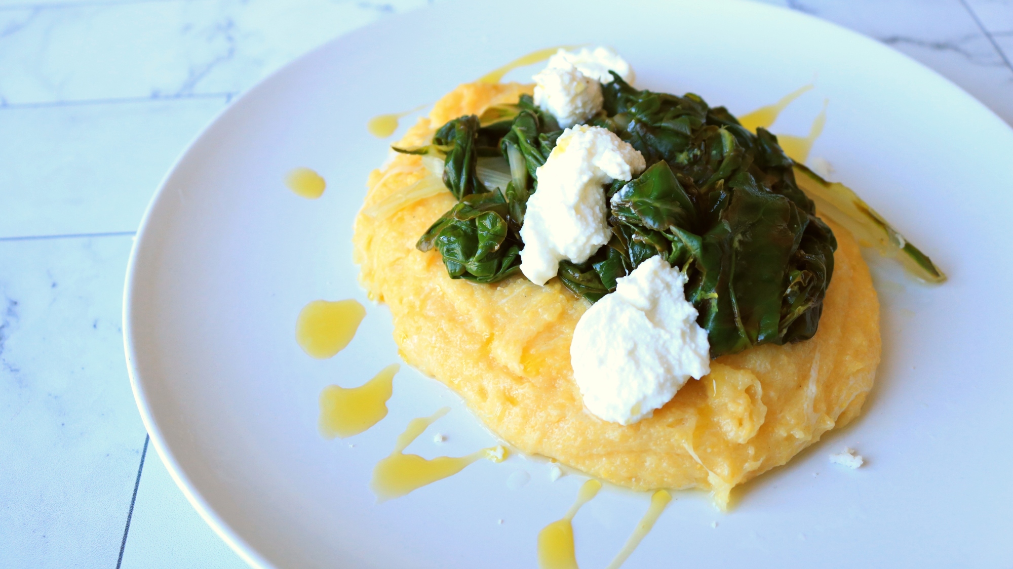 A plate of yellow polenta and dark greens on top.