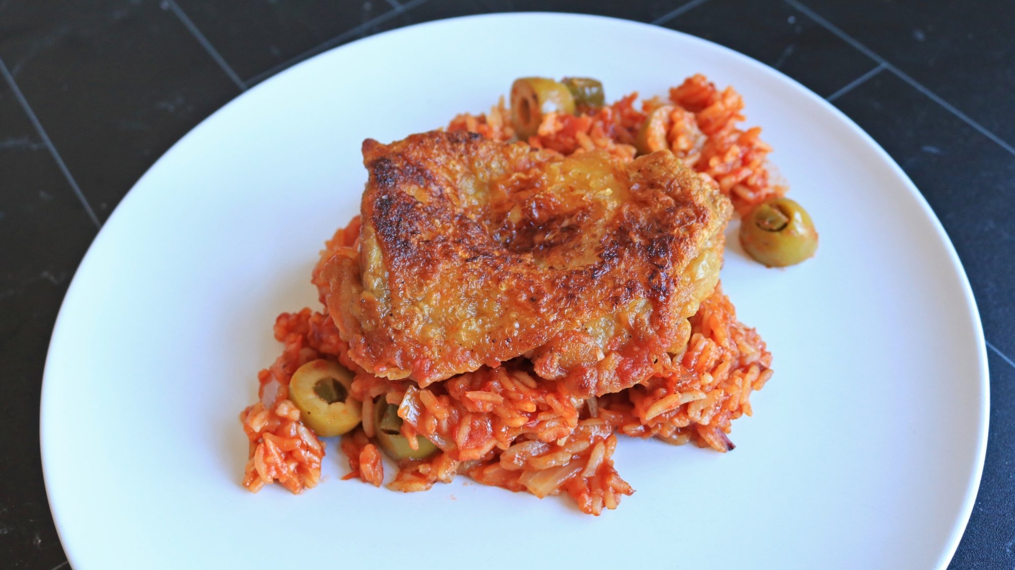 A chicken thigh on a pile of tomato rice.