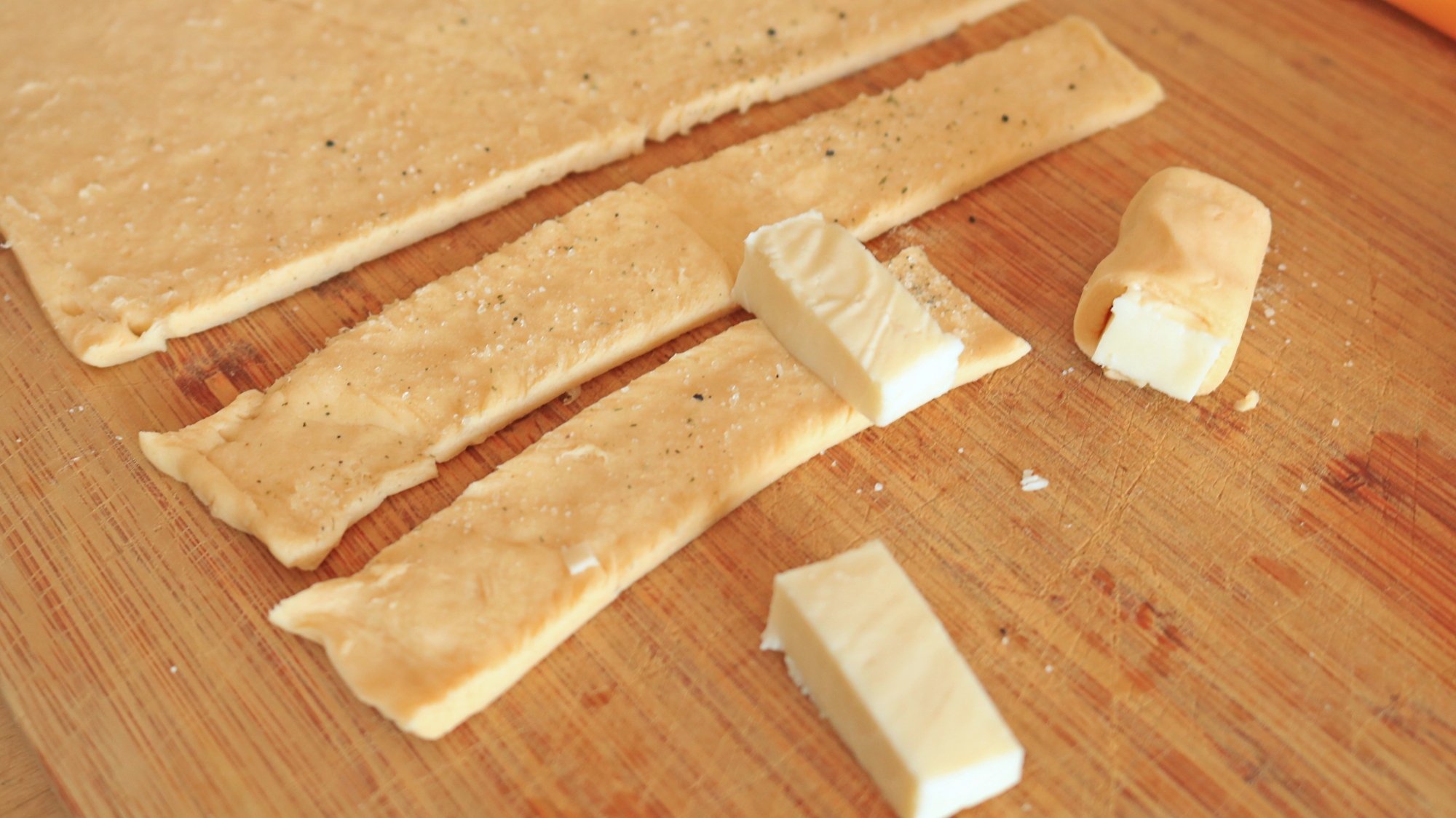 Small pieces of cheese being wrapped in seasoned Pillsbury crescent dough.