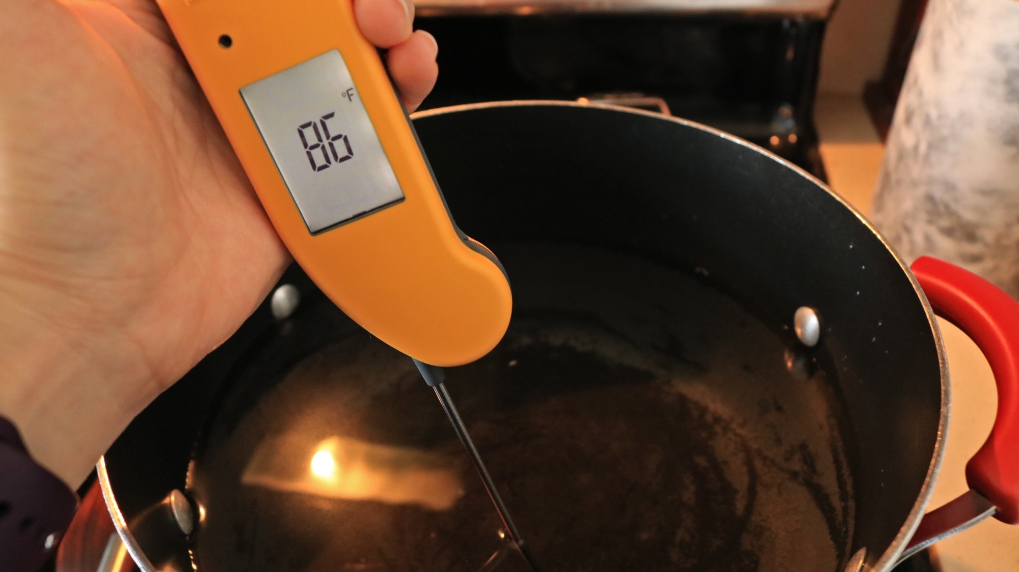 A hand holding an thermometer in water reading eighty-six degrees.