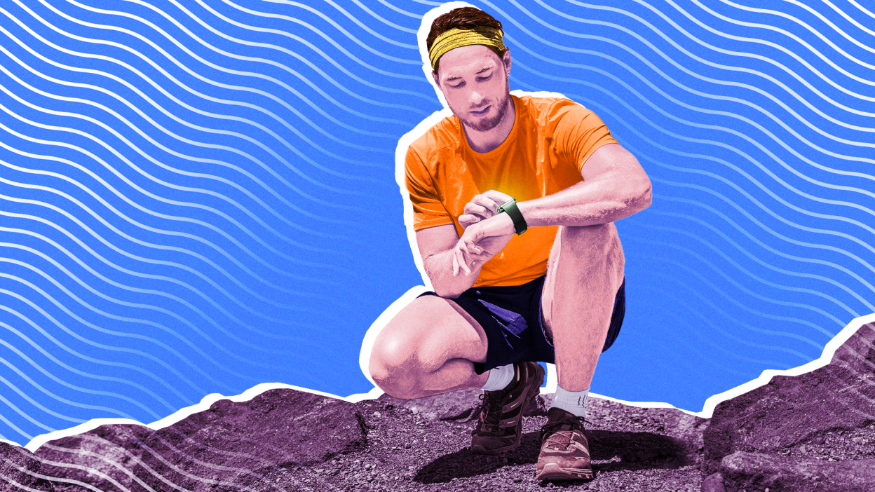 A man kneeling on a rocky surface and checking his fitness tracker