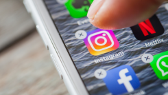 A finger hovering over the Instagram app on their iPhone, preparing to delete it