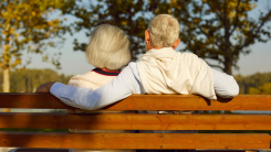 Back view of mature senior couple family sitting on the bench in park and hugging enjoying retirement and spending time together in nature