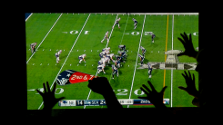 The Super Bowl playing on a flatscreen TV in a dark room with viewers visible cheering in front of it