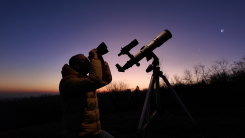 Person looking at the night sky with binoculars and a telescope