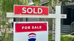 A "sold" sign above a realtor's sign in a yard
