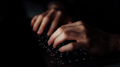 Close-up image of a computer keyboard with hands typing in dim light