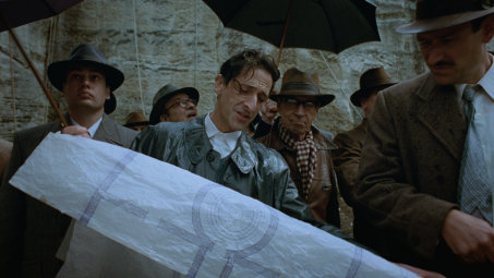A still from The Brutalist showing Adrian Brody holding a blueprint for a circular building