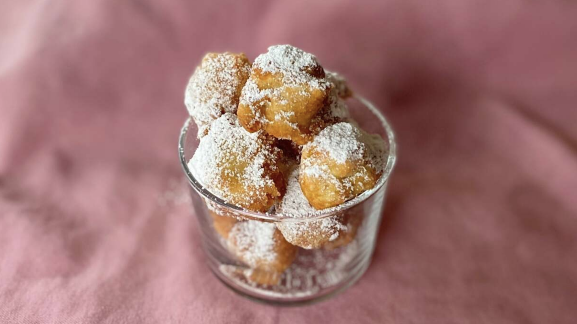 A glass cup full of friend dough topped with powdered sugar.