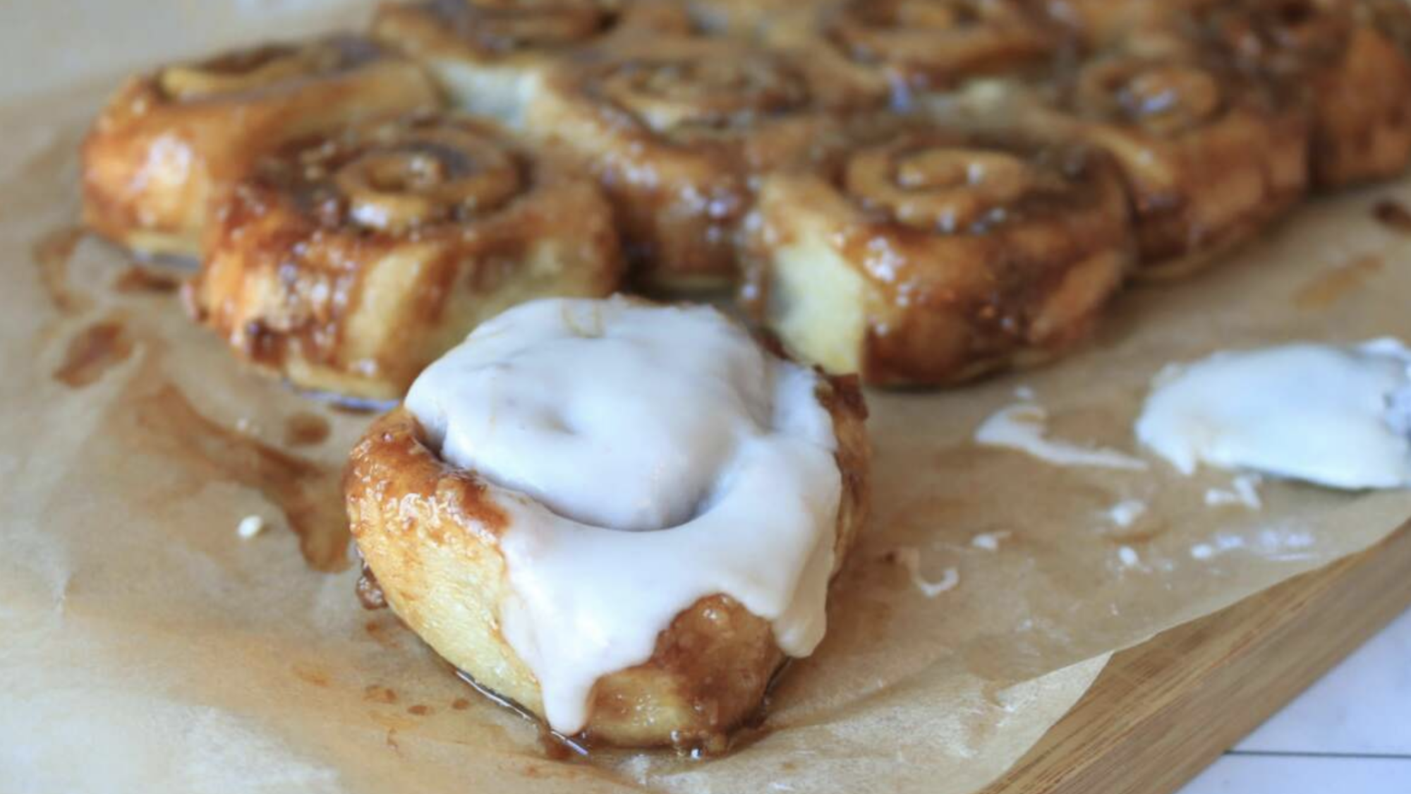 A batch of cinnamon rolls on a table, one has icing on it.