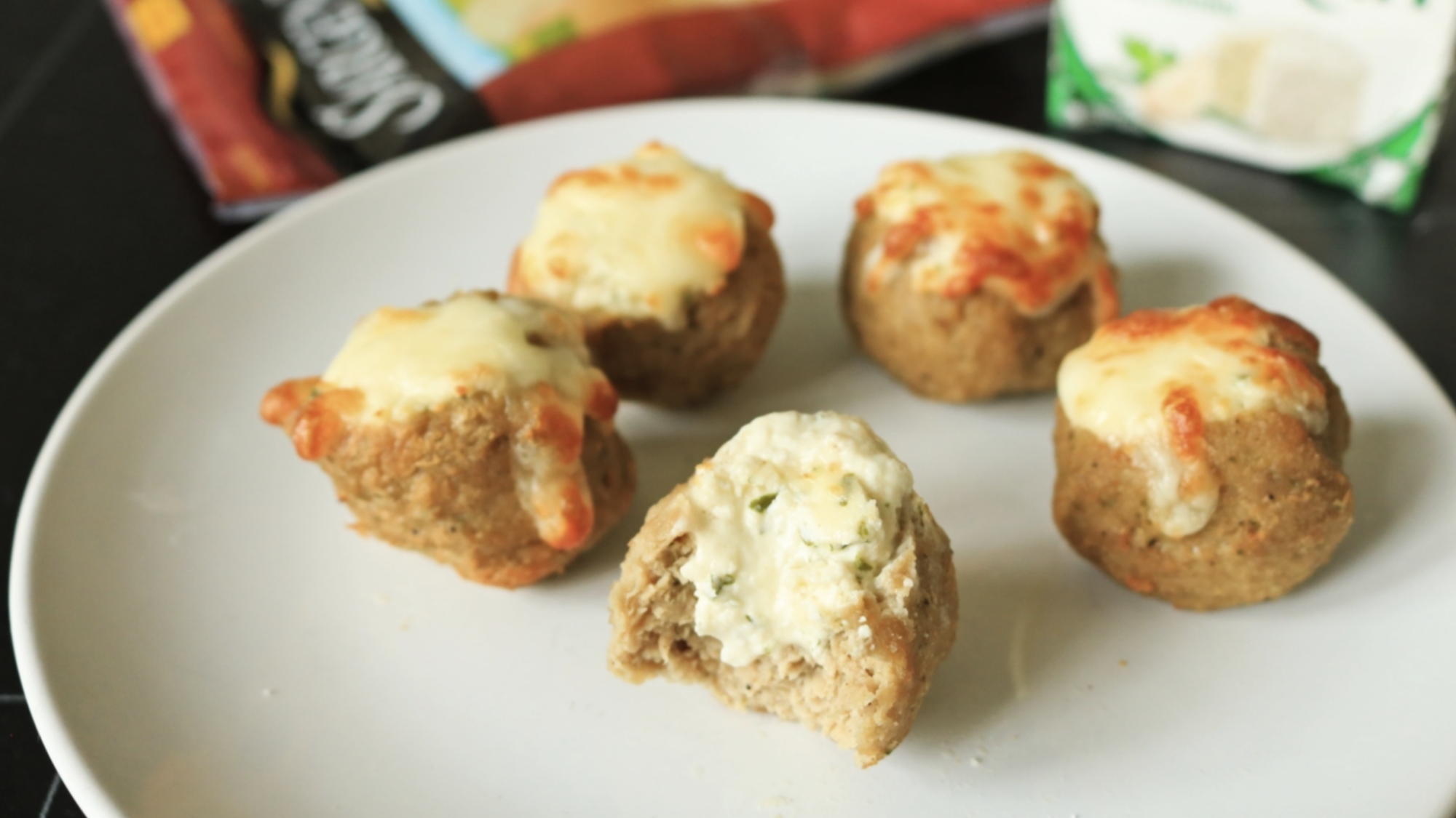Meatballs with cheese on top of a white plate.