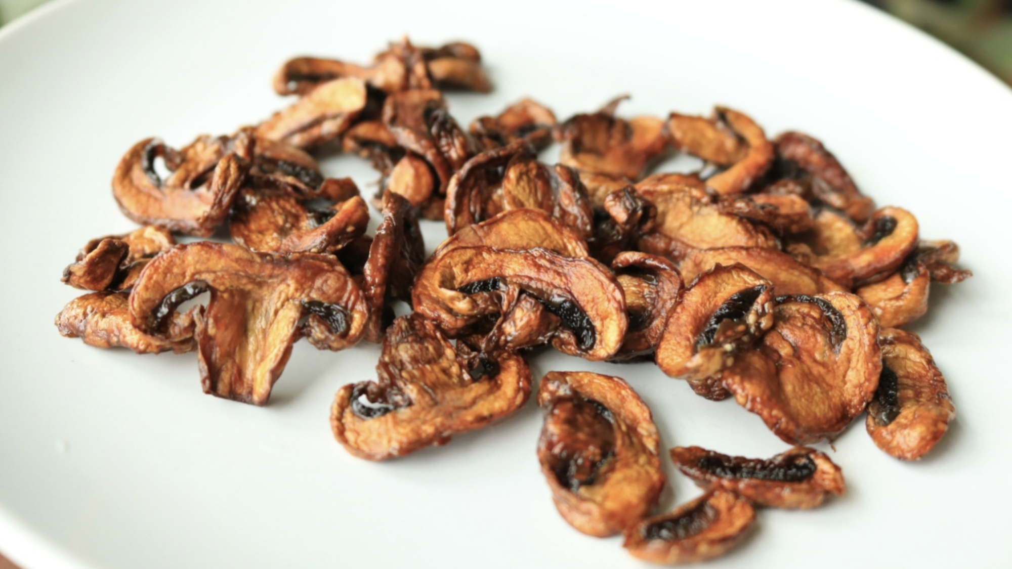 Mushroom chips in a pile on a white plate.
